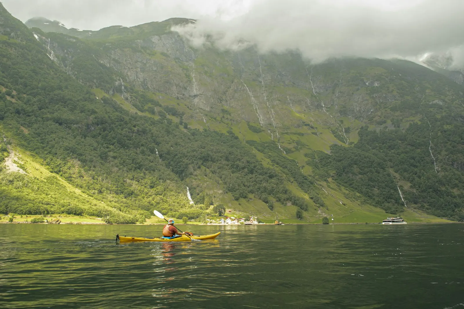 En padler i gul kajakk på Nærøyfjorden ved Gudvangen, under grønne fjellsider med fossefall
